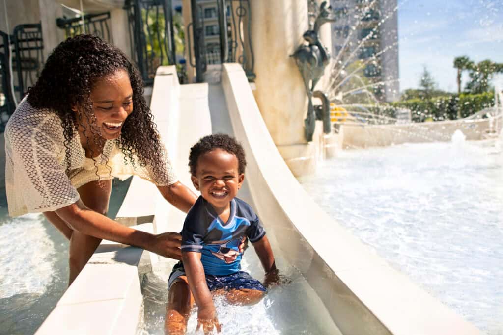 Mom catching toddler at the end of the slide at a disney pool