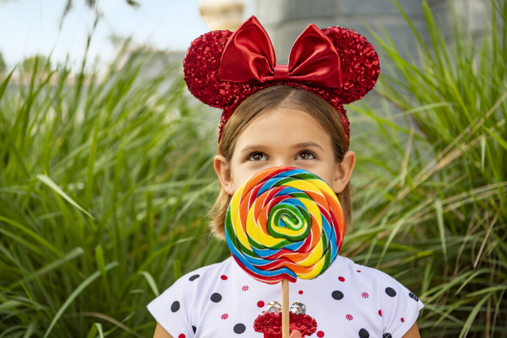 Young girl wearing Mickey ears holding a lollipop snack