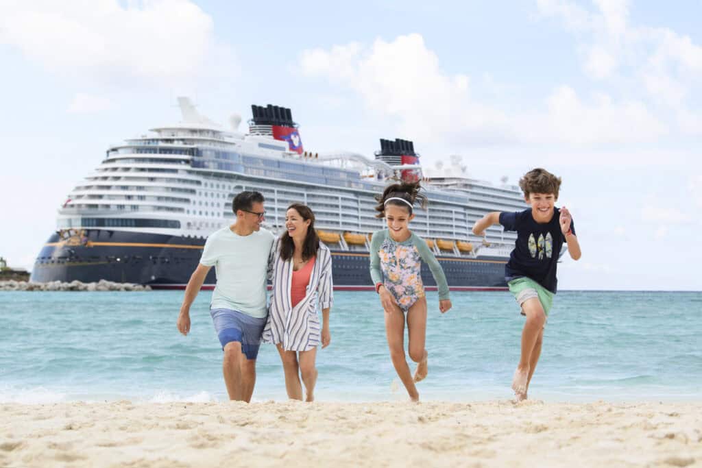 Family smiling running on beach in front of Disney cruise ship