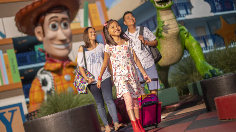 Family smiling pulling luggage through All Star Movie Resort at WDW